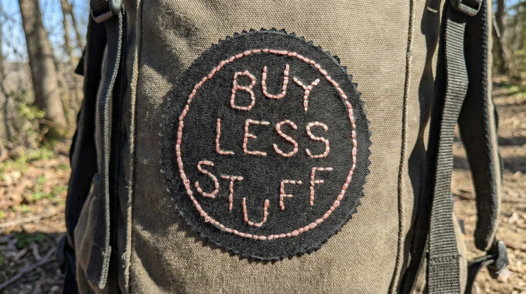 hand stitched patch that reads 'buy less stuff' on a rucksack in the woods